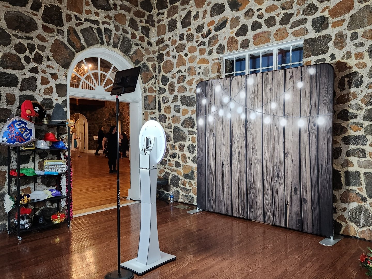 Open-air booth with a wood-panel backdrop and prop display in a stone hall