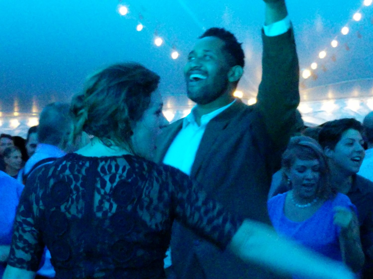 Guests cheering with hands raised on a tented dance floor washed in blue light