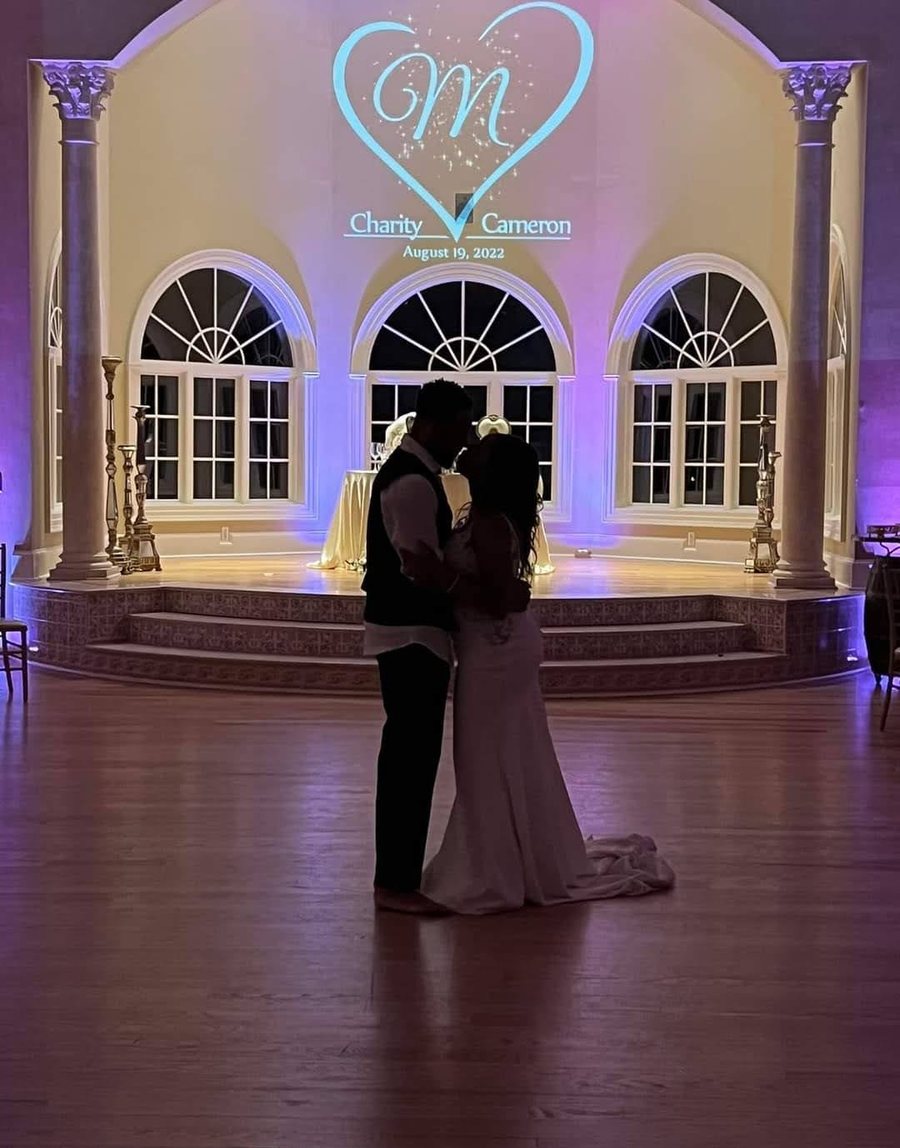 Couple dancing beneath a projected heart monogram in a candlelit ballroom