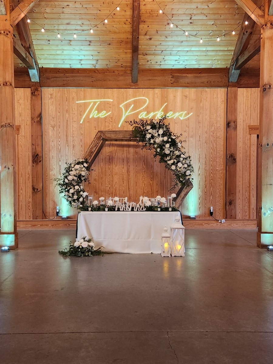 Barn sweetheart table under a custom neon name sign with teal uplighting