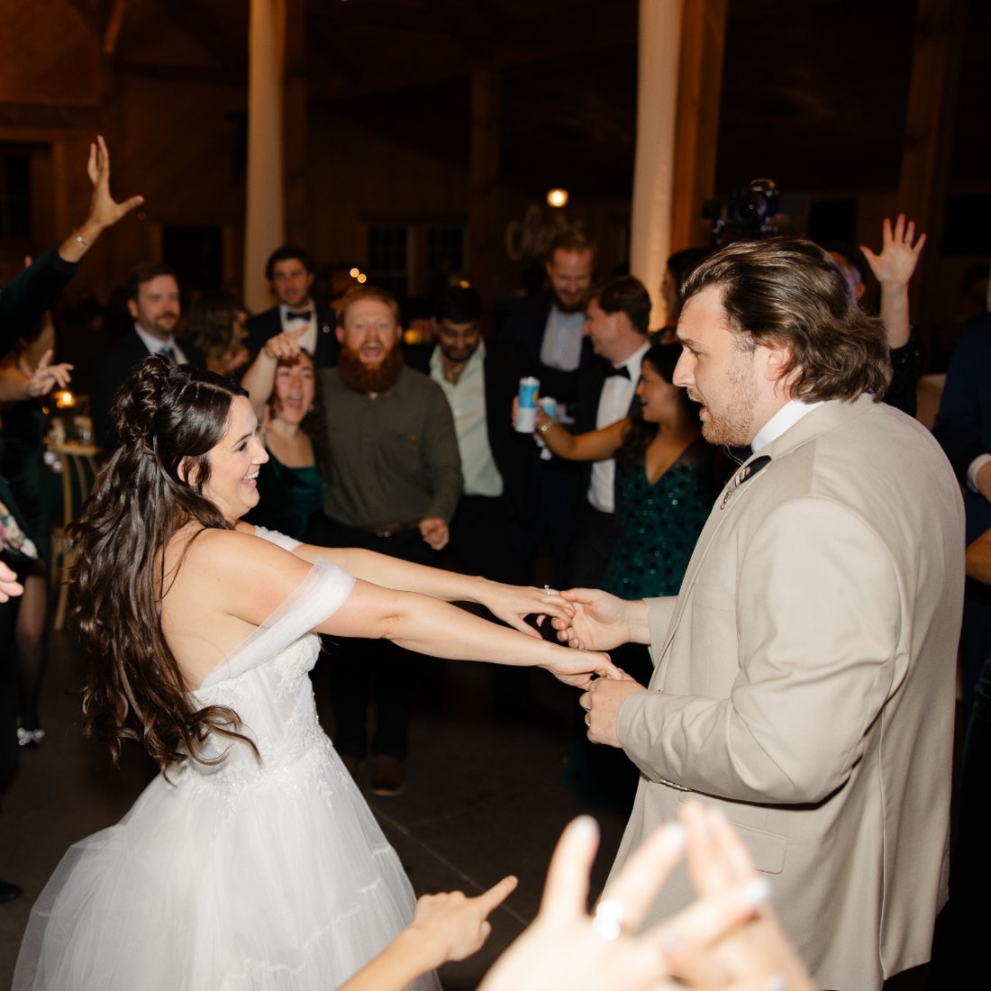 Bride dancing hand in hand with a guest as the crowd cheers around them