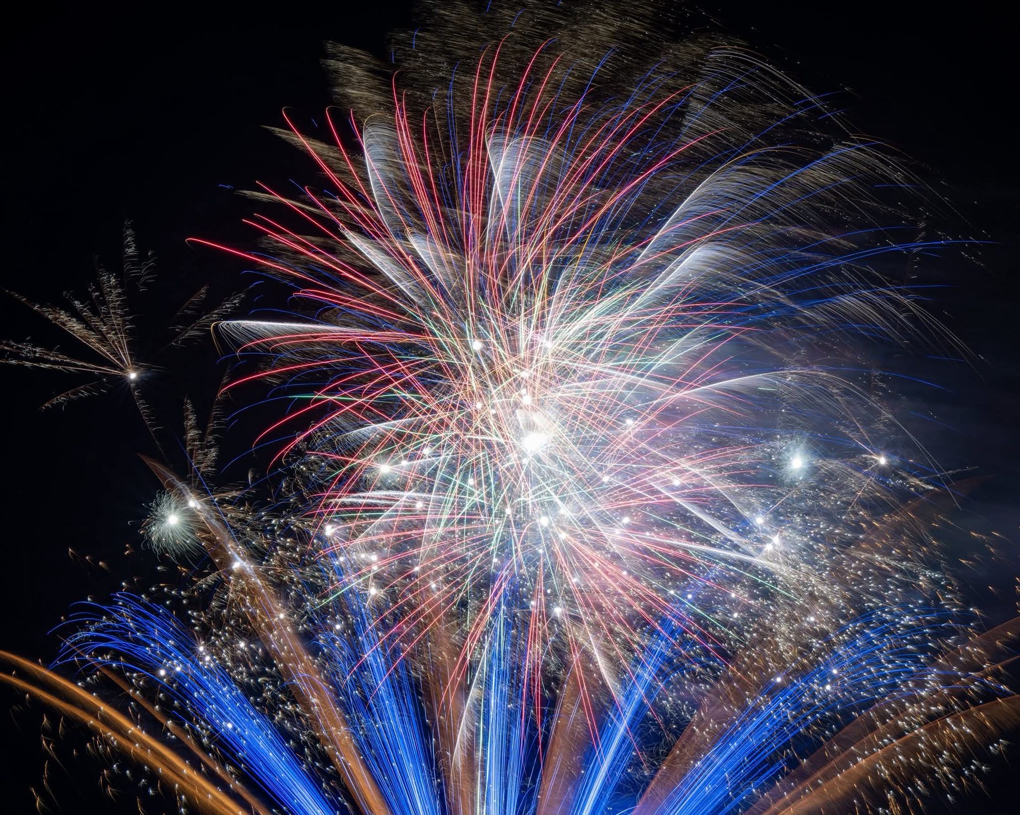 Large gold and white fireworks burst over a wedding venue at night