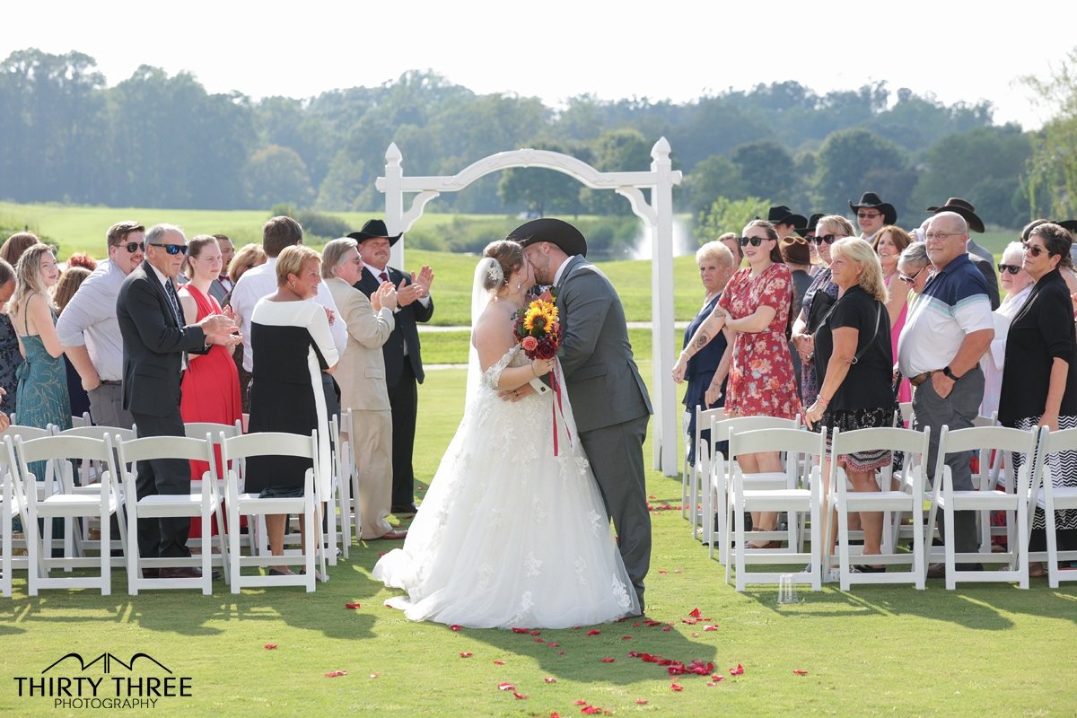 Couple kissing at the end of an outdoor ceremony aisle